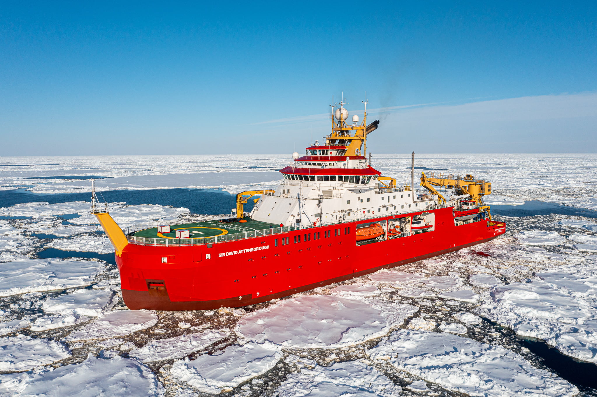 A large red ship sails through water covered in large and small pieces of sea ice.