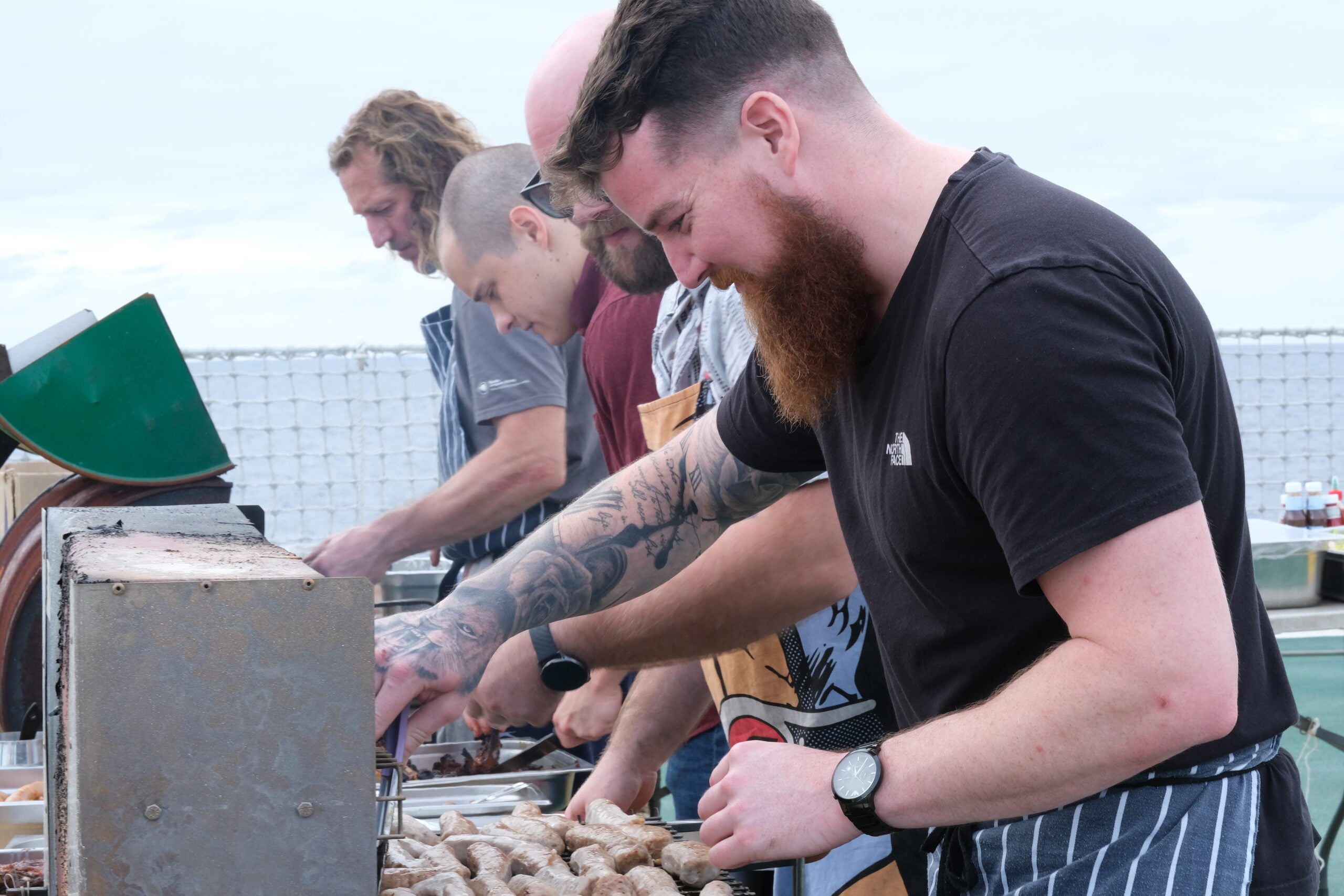 Four men cook over a BBQ on the deck of a ship