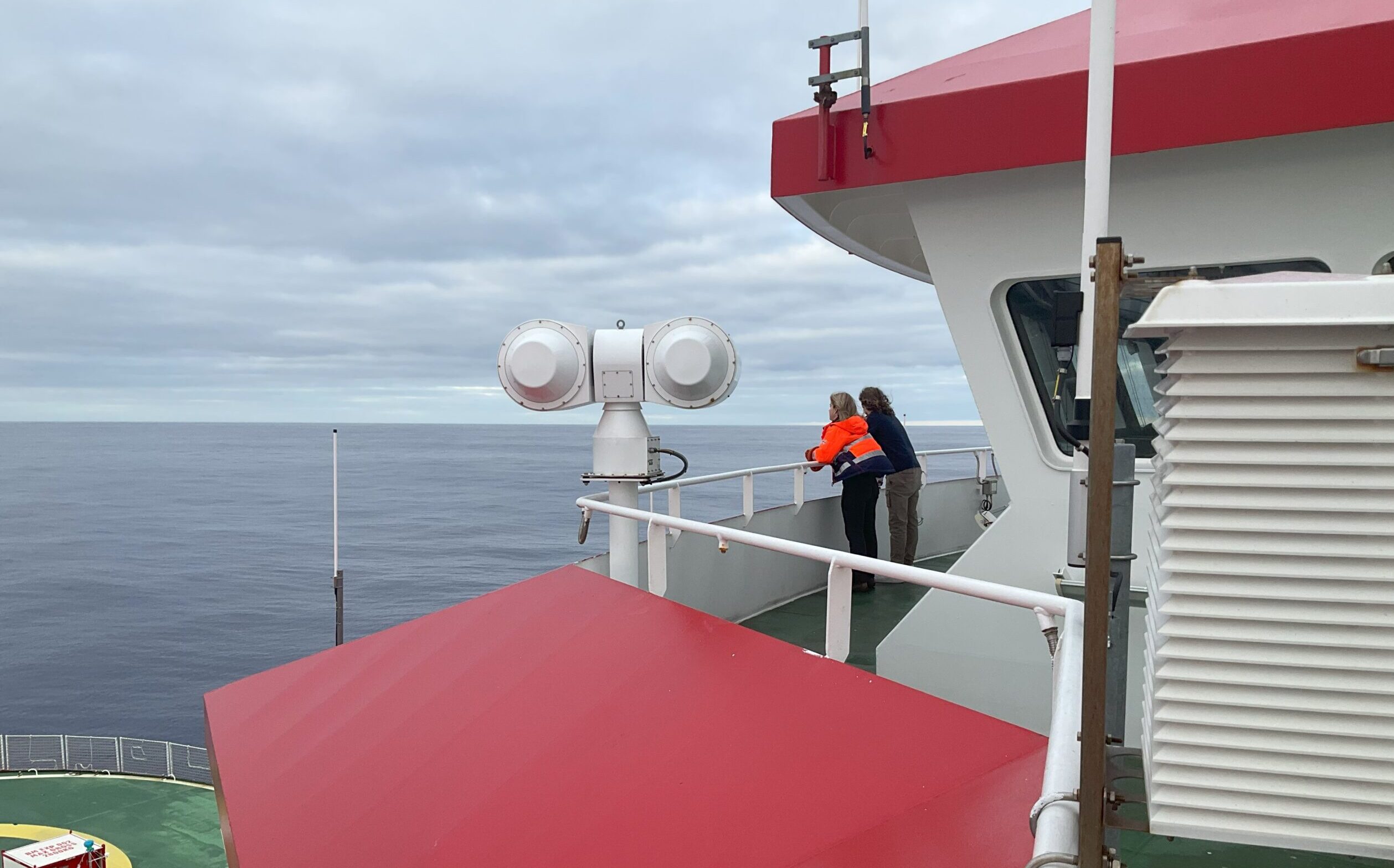 Two people look to sea from the top deck of the ship