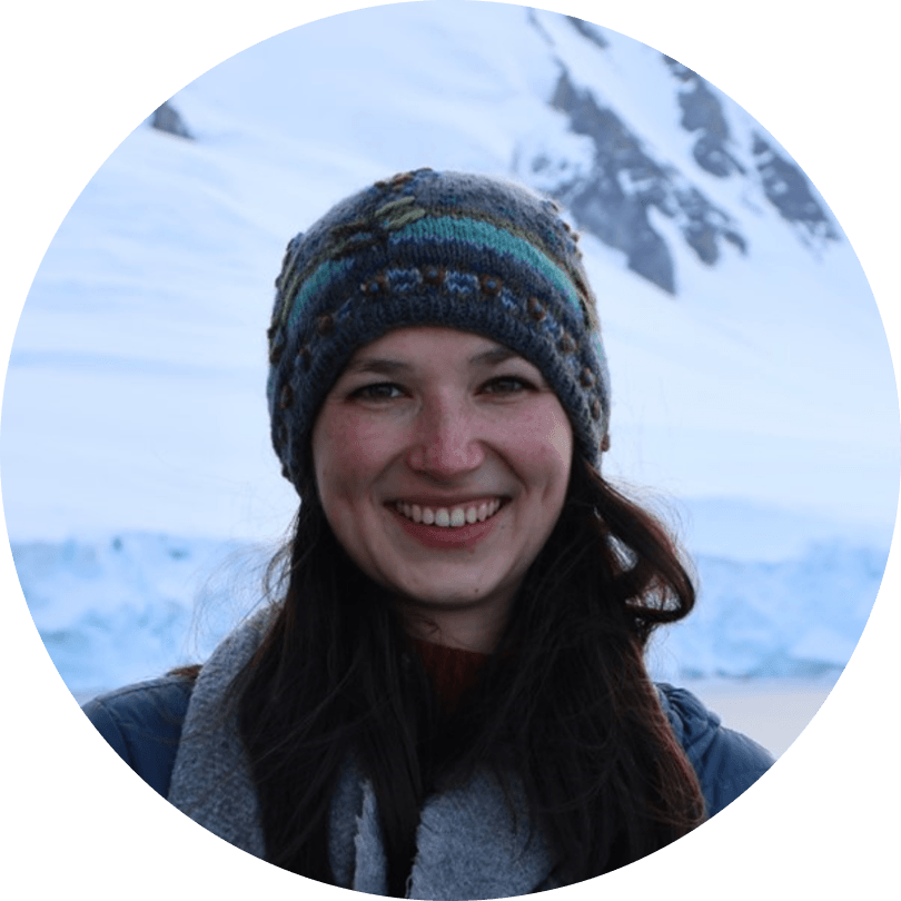 A woman in a hat and scarf smiles at the camera