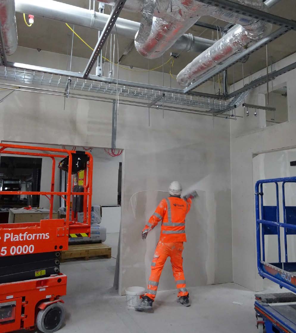 A man in an orange boiler suit plasters a wall