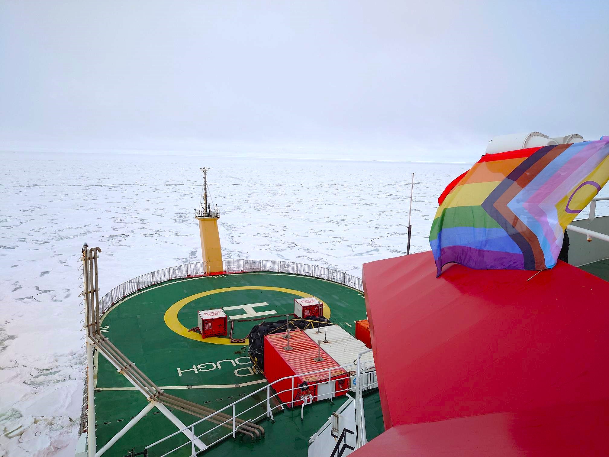 A Pride flag on a ship surrounded by sea ice