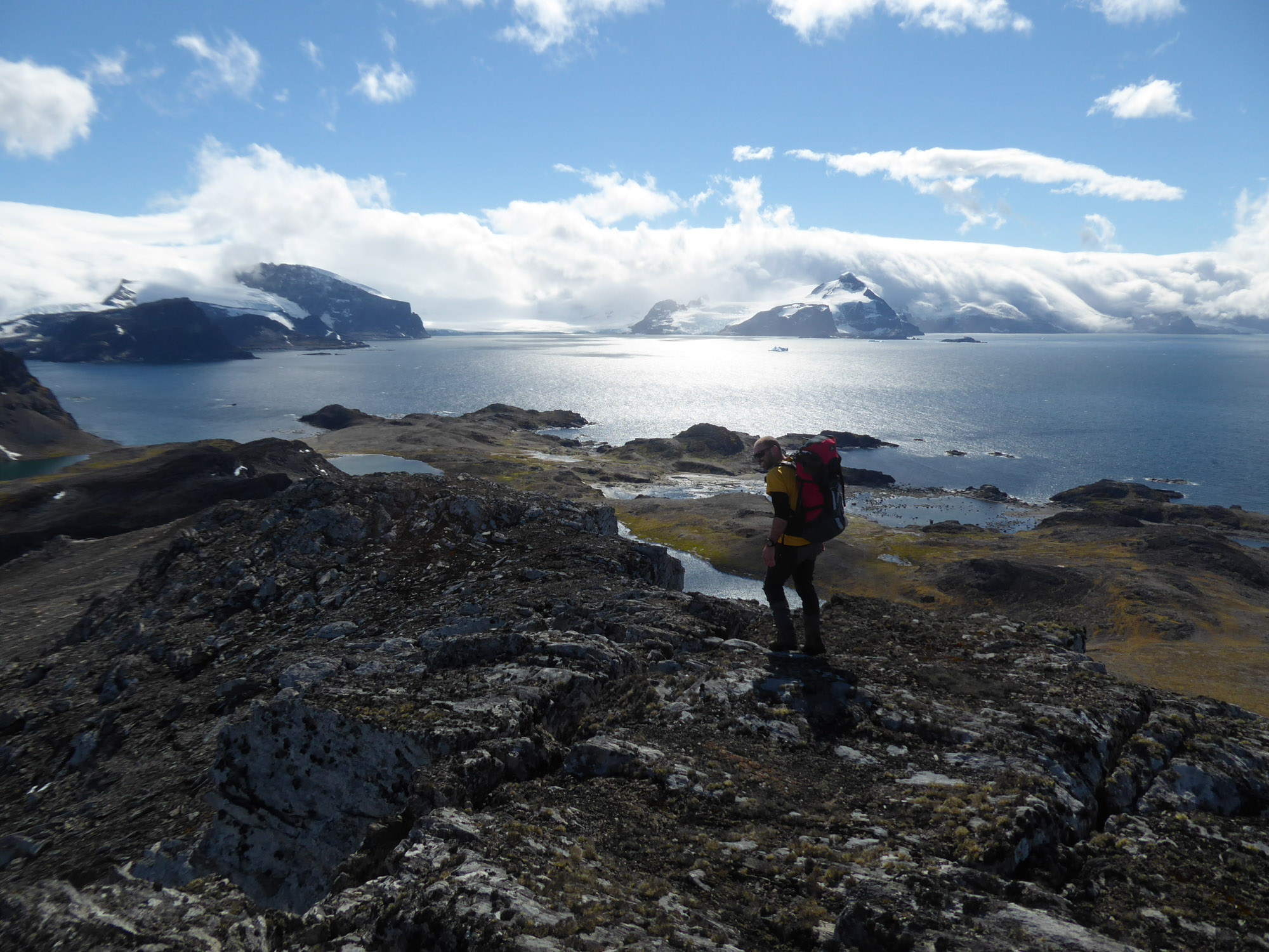 A man in hiking clothes with a large rucksack walking across rocky ground