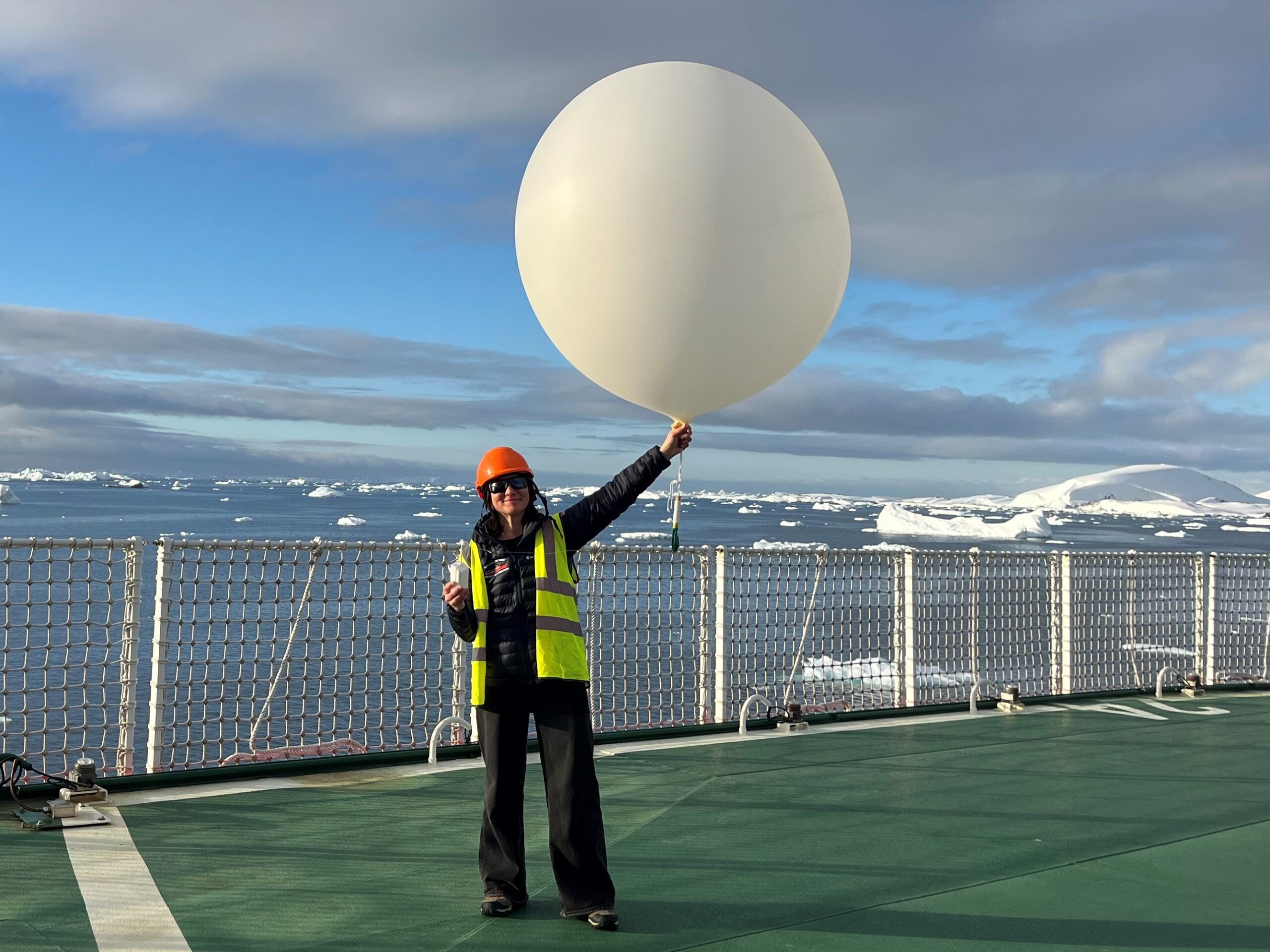 A woman stands on a ship holding a giant white balloon