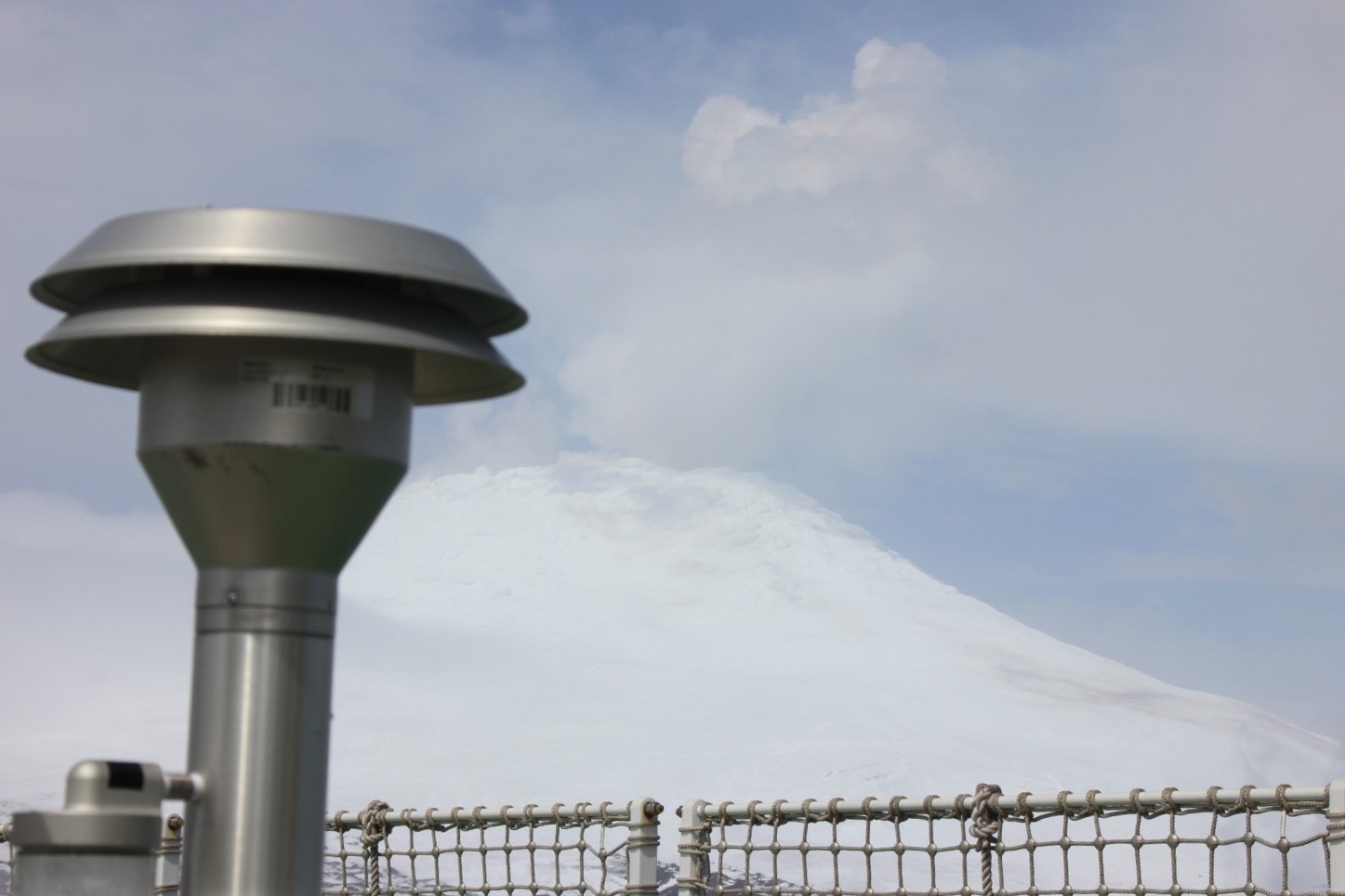 A vertical metal tube with a wide opening on the top with clouds and snowy mountain in the backgroud