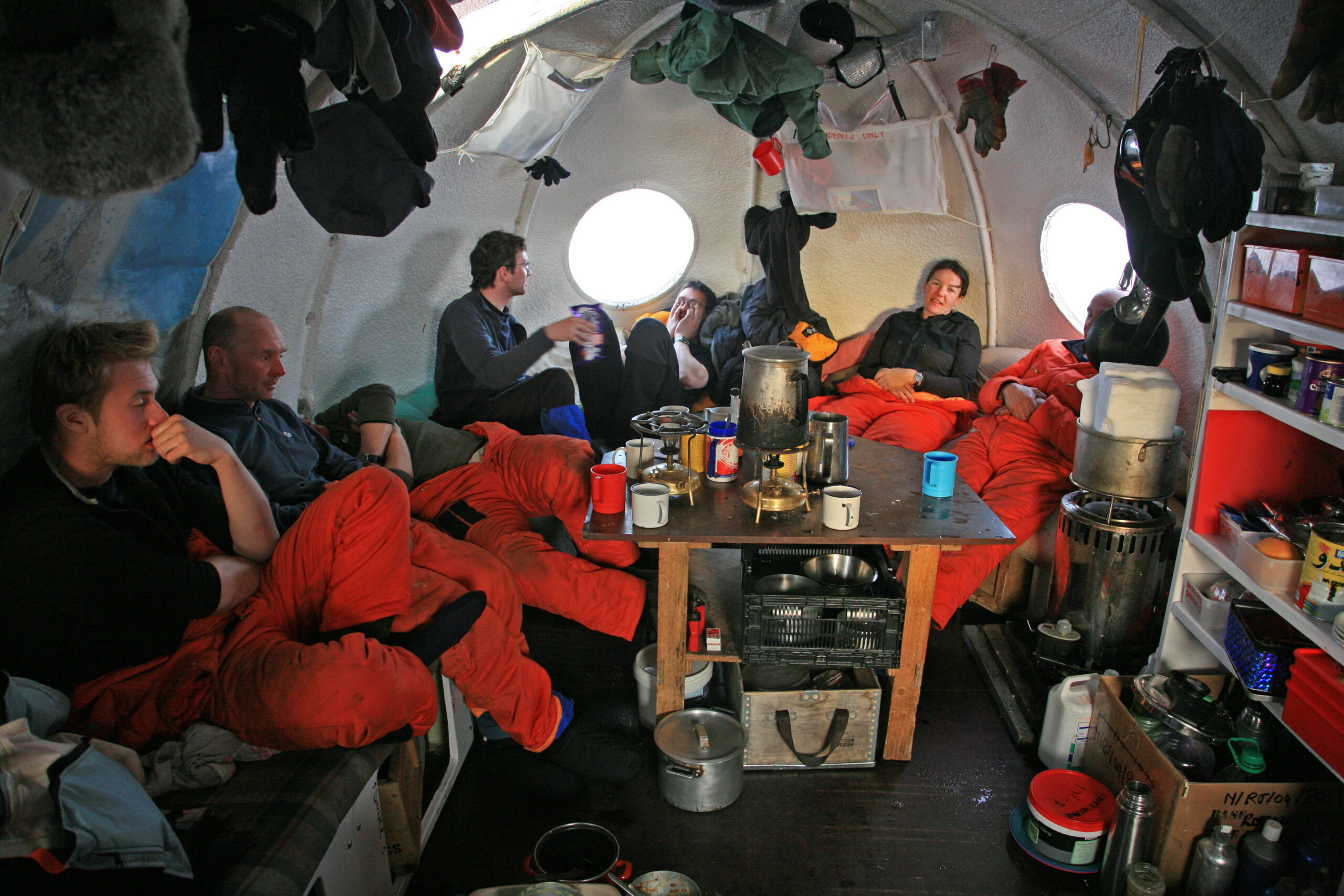 A group of people sitting in a tent around a table, chatting