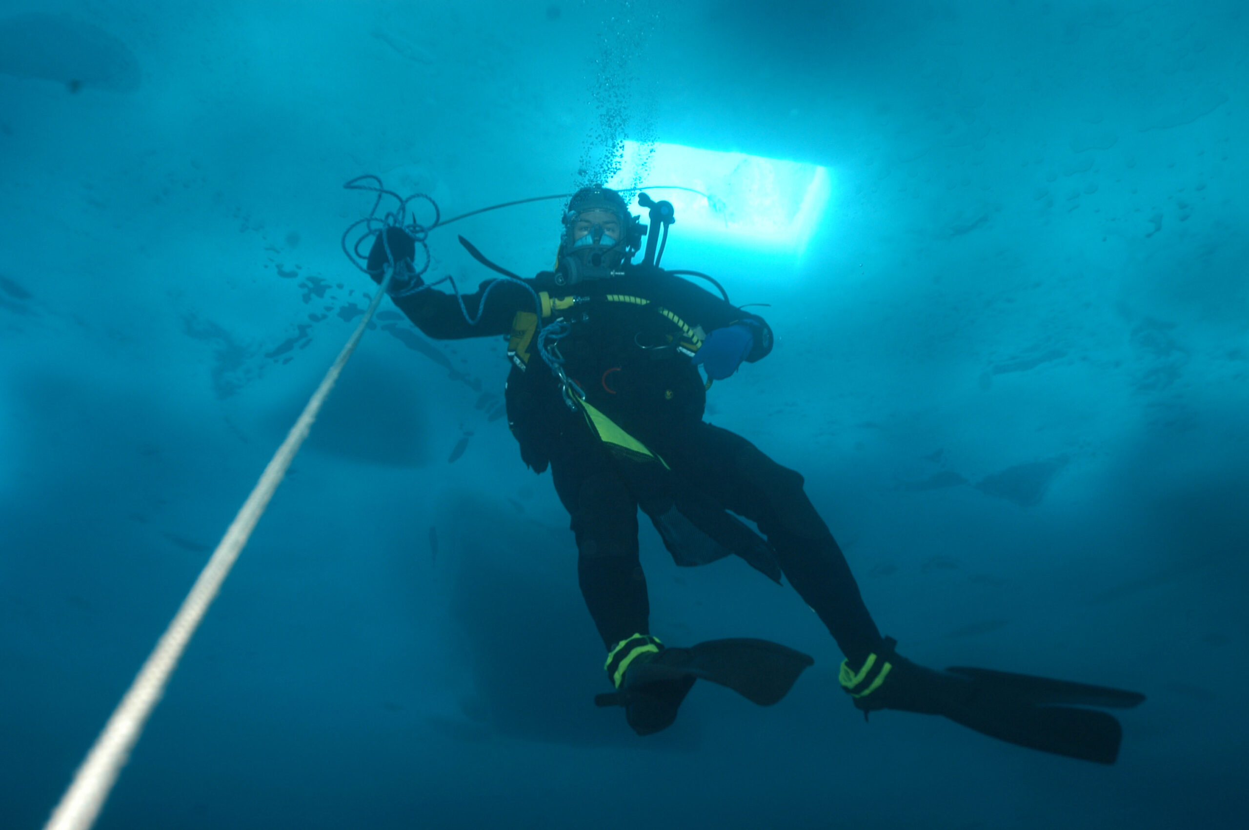 A diver ascends up a lifeline towards a hole in the ice