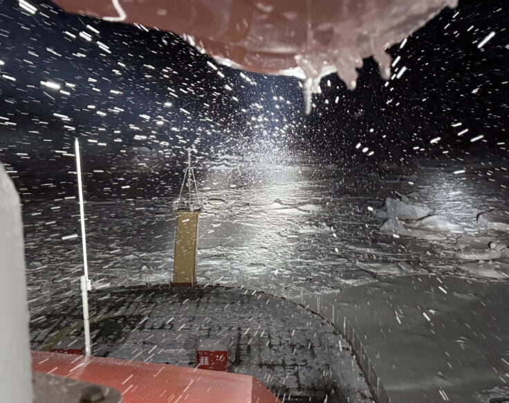 View over the front of a ship as it navigates through a blizzard and sea ice in the dark