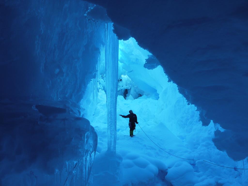 A person bathed in bright blue light inside a crevasse