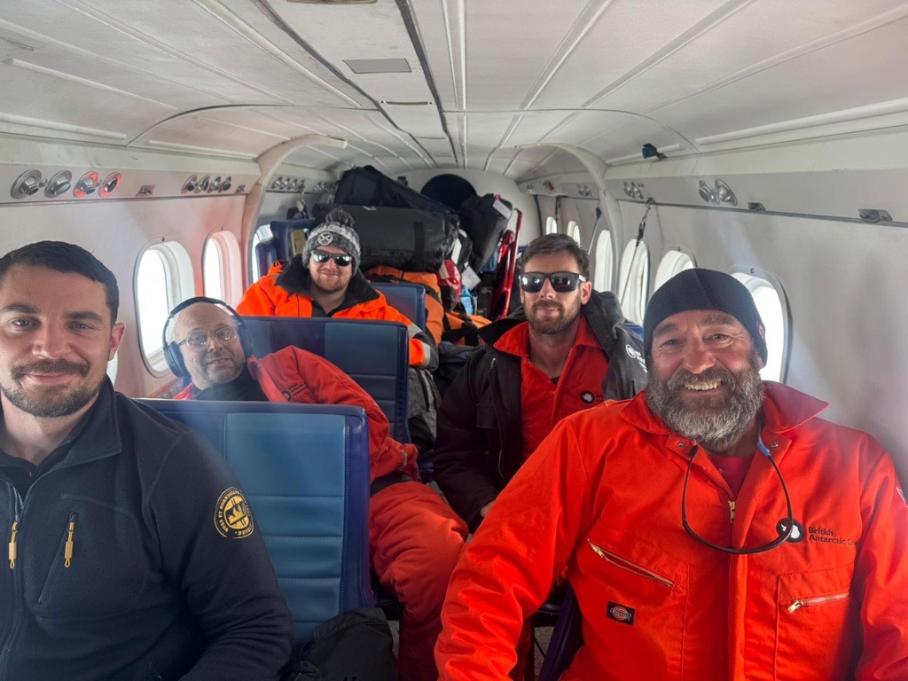Four mean sat in a small plane, smiling at the camera