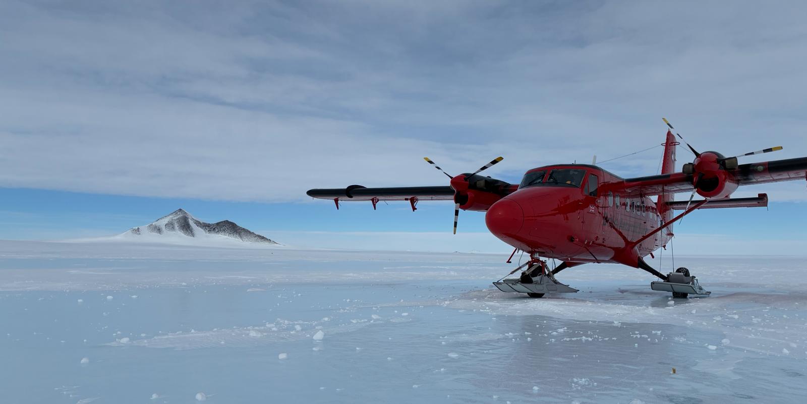 A small red plane on skis on a field of ice