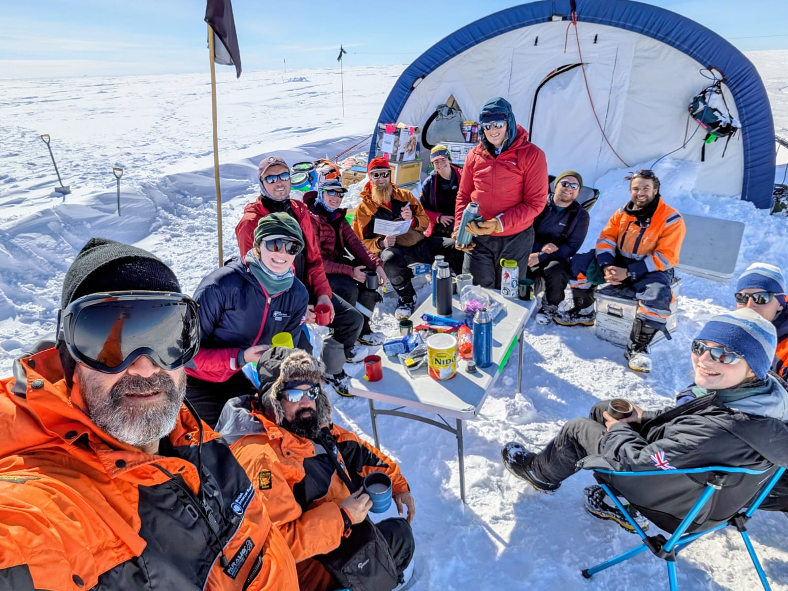 A group of people sitting in the snow, having a tea break