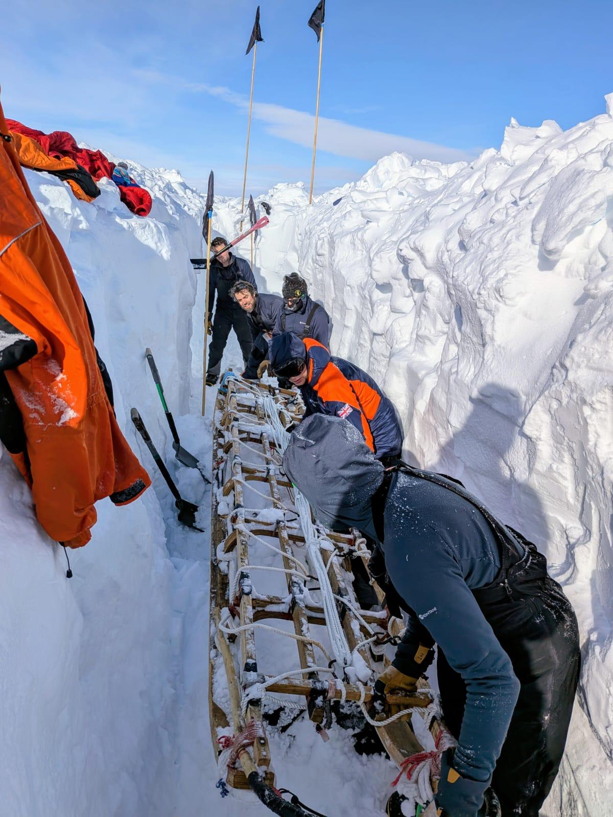 A group of people in a deep channel of snow, lifting out a sledge
