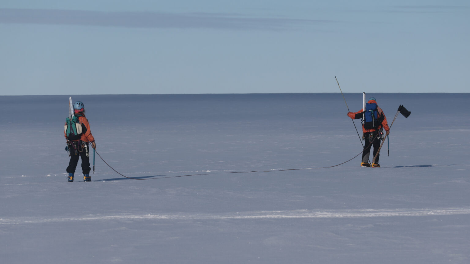 Two people tethered together walking across an open expanse of ice