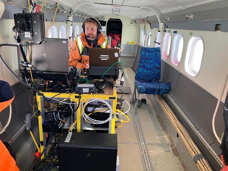 A man sits in a small plane looking at different screens connected to science instruments