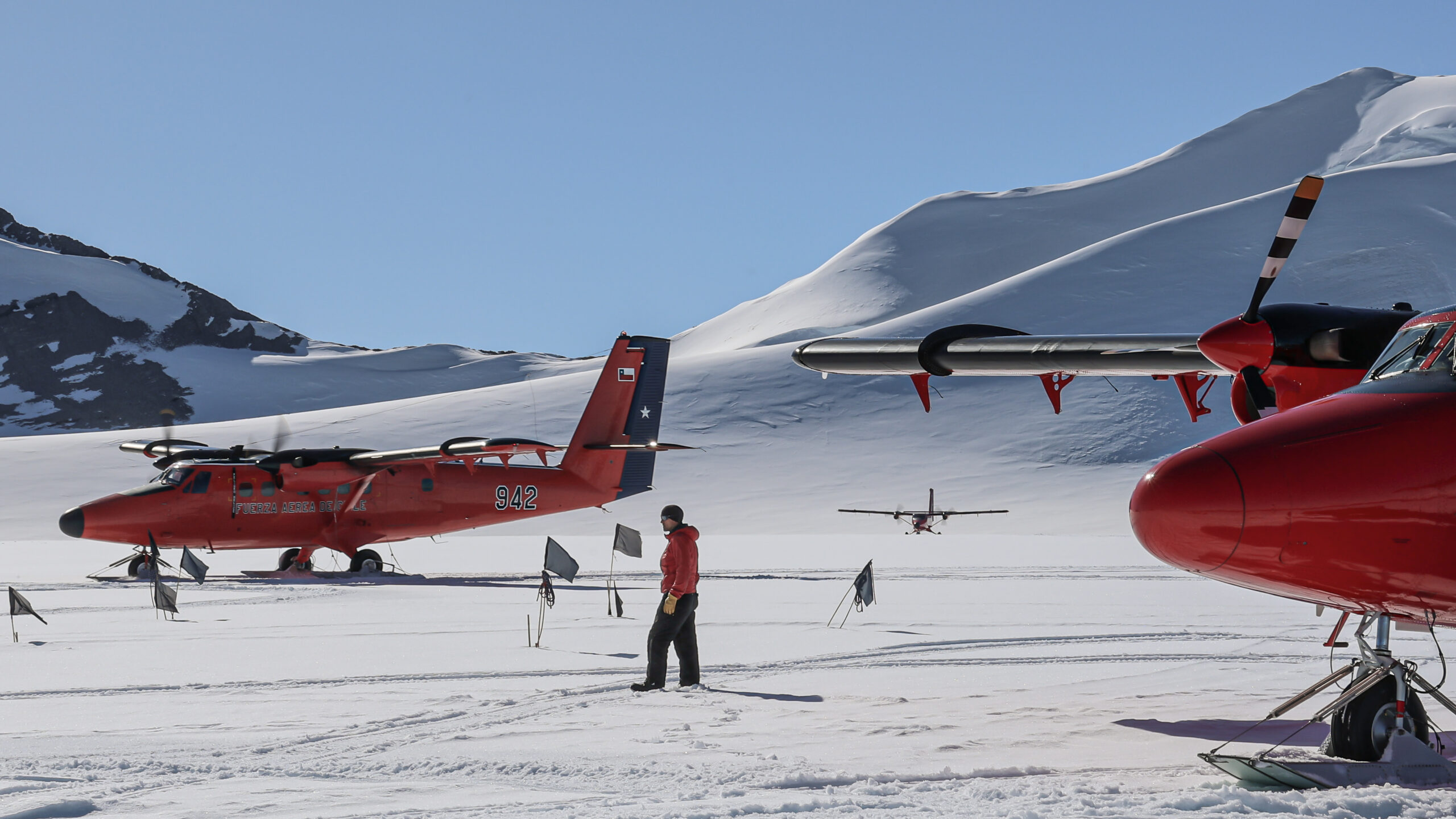 A man stands in as snowy landscape surrounded by three small red planes